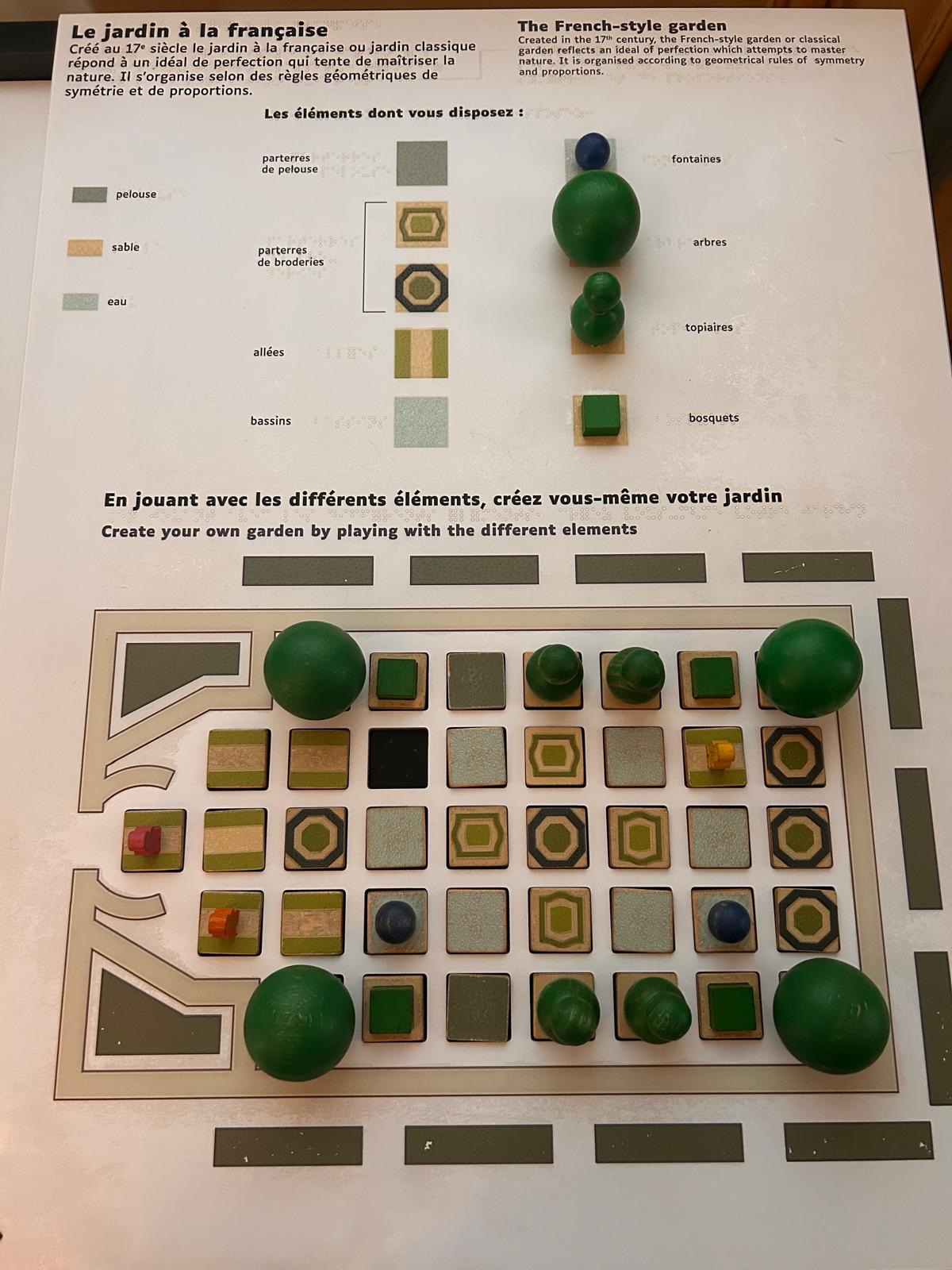 Une maquette tactile avec des pièces amovibles représentant les différents éléments d'un jardin classique : parterres, fontaines, arbres et allées.