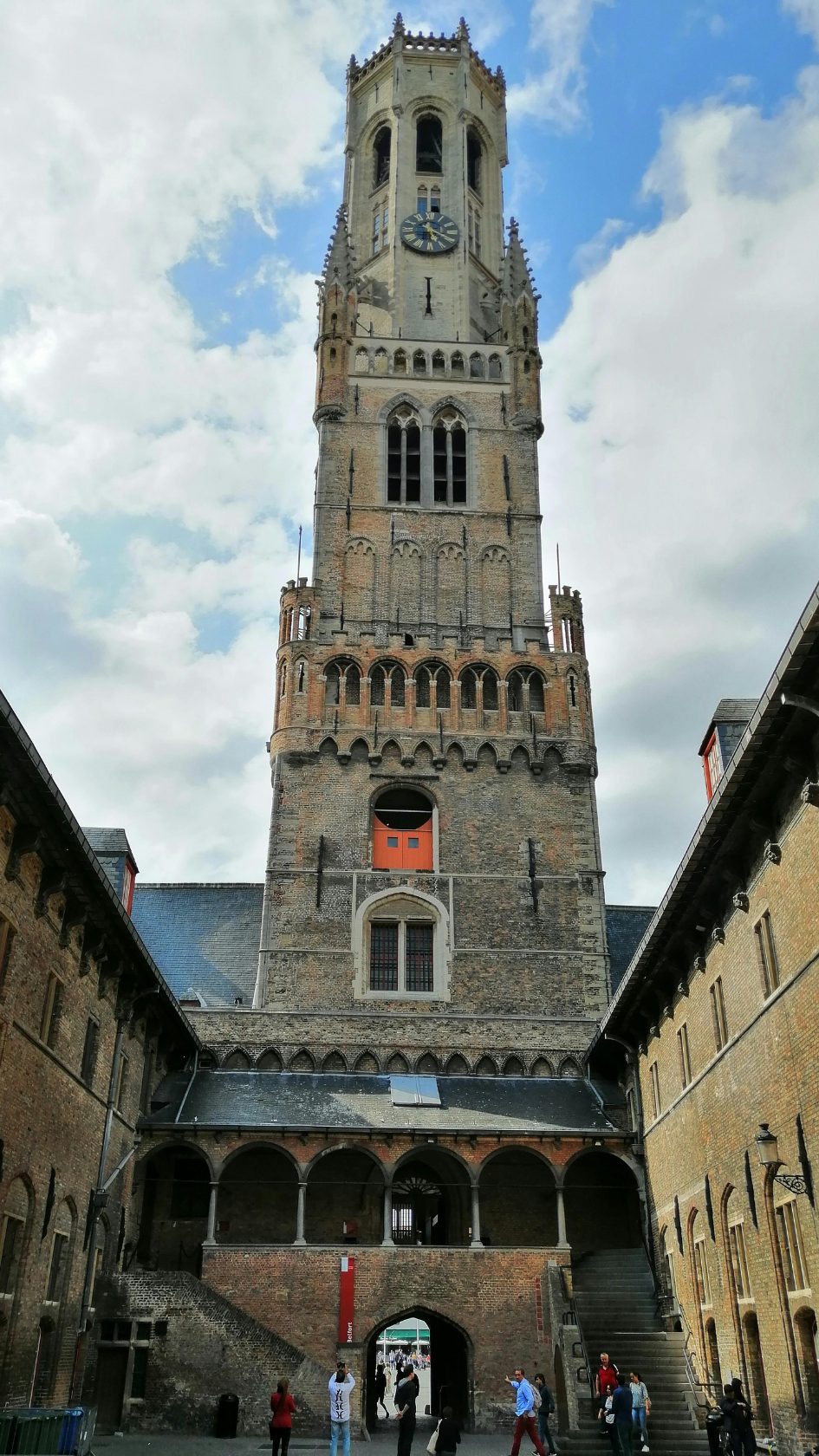 Vue du beffroi médiéval de Bruges depuis la cour intérieure, symbole d'un patrimoine touristique historique accessible.