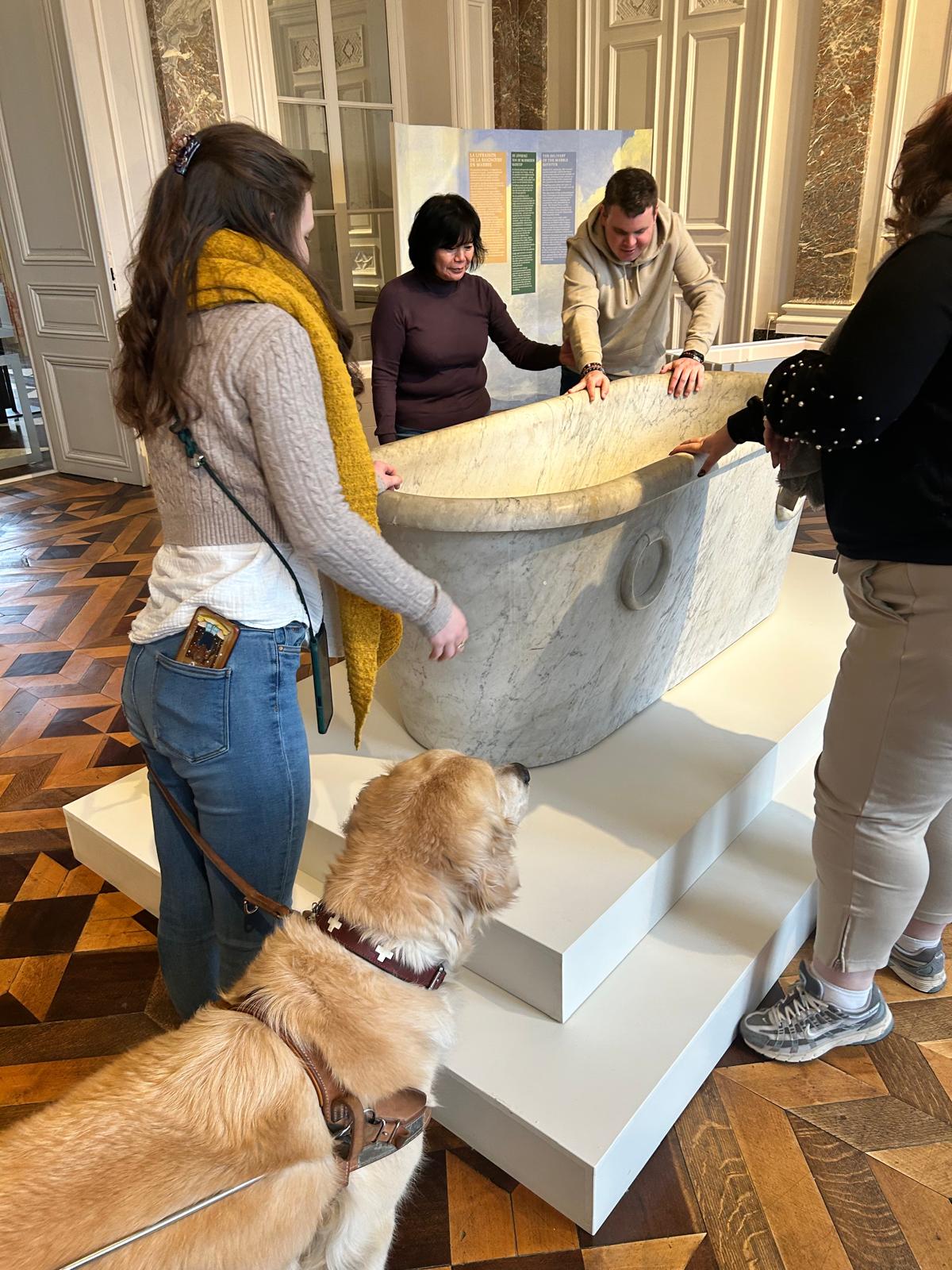 Un groupe avec chien d'assistance explore une maquette tactile en musée.